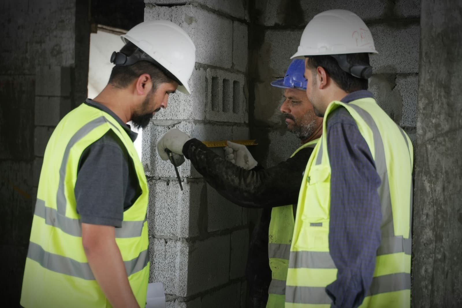 Three workers in hard hats measuring a concrete block wall together