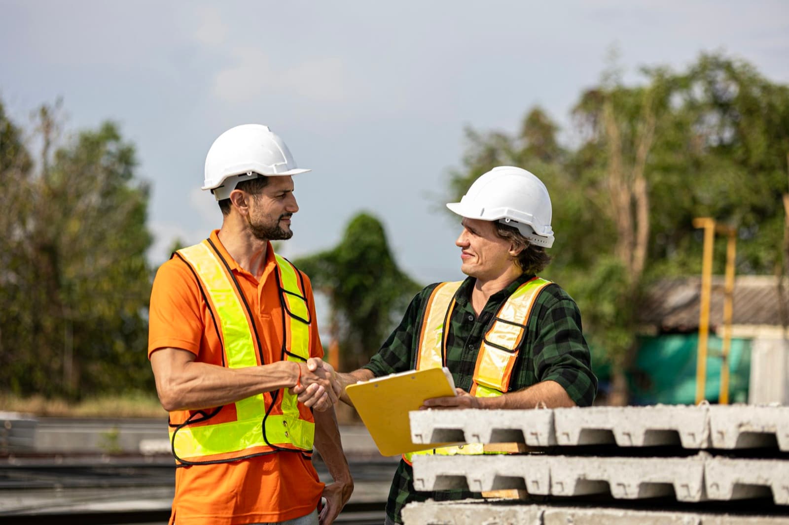Two construction workers in hard hats and safety vests shaking hands on a job site